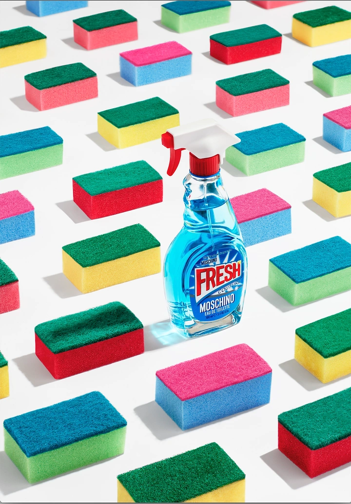 Fashion creative ad: Perfume shaped like a glass-cleaner spray bottle among rows of colorful sponges