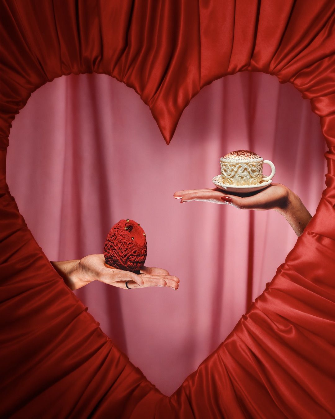 Two hands offering a red dessert and a cappuccino-style cup inside a satin heart