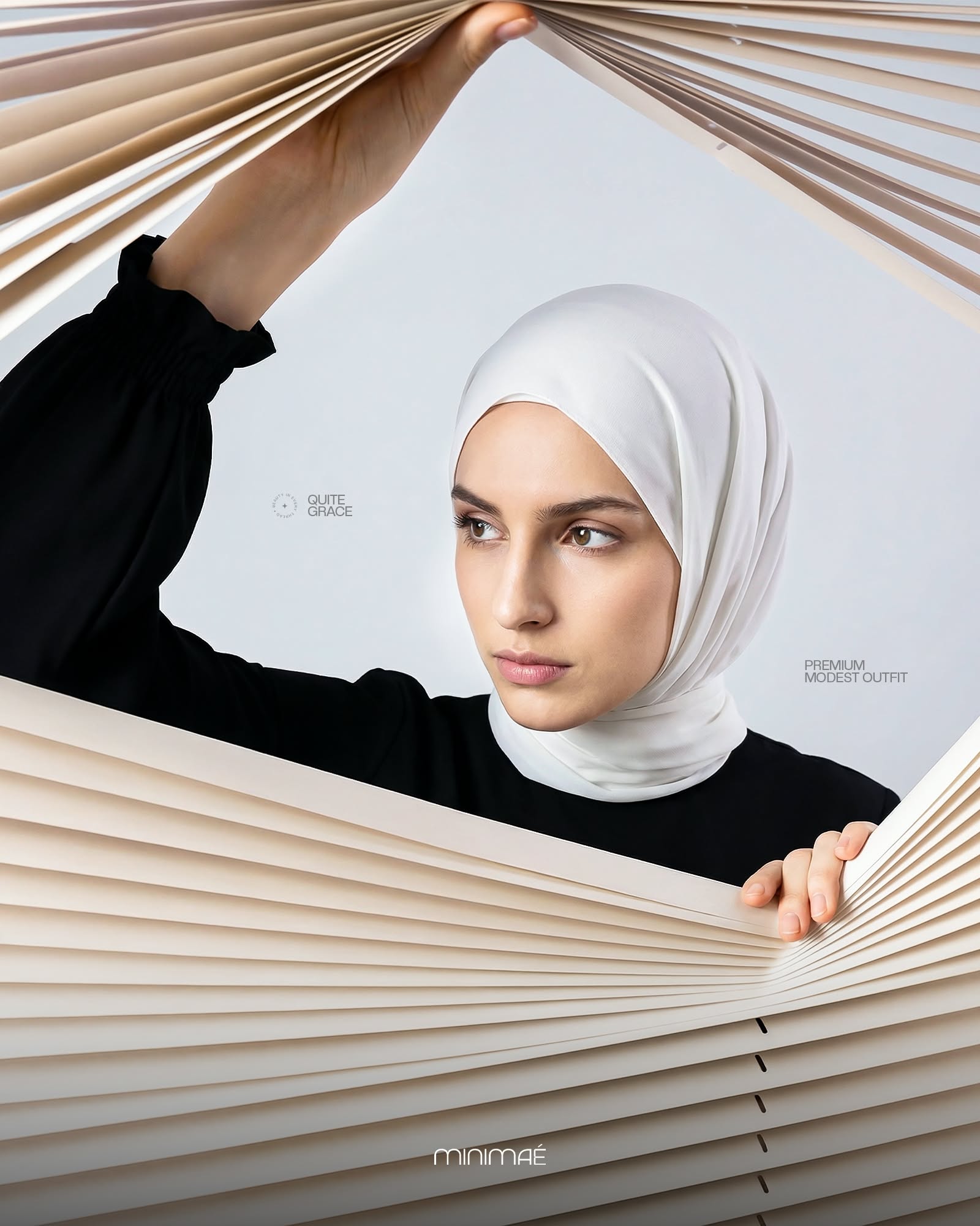 Instagram post: Model in a white hijab and black dress peering through parted cream blinds