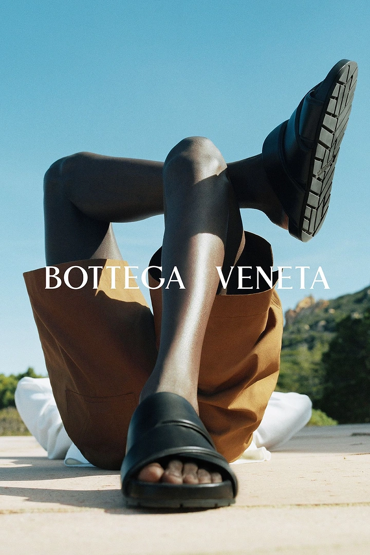Creative ad: Low-angle shot of a reclining model's legs wearing black rubber slides