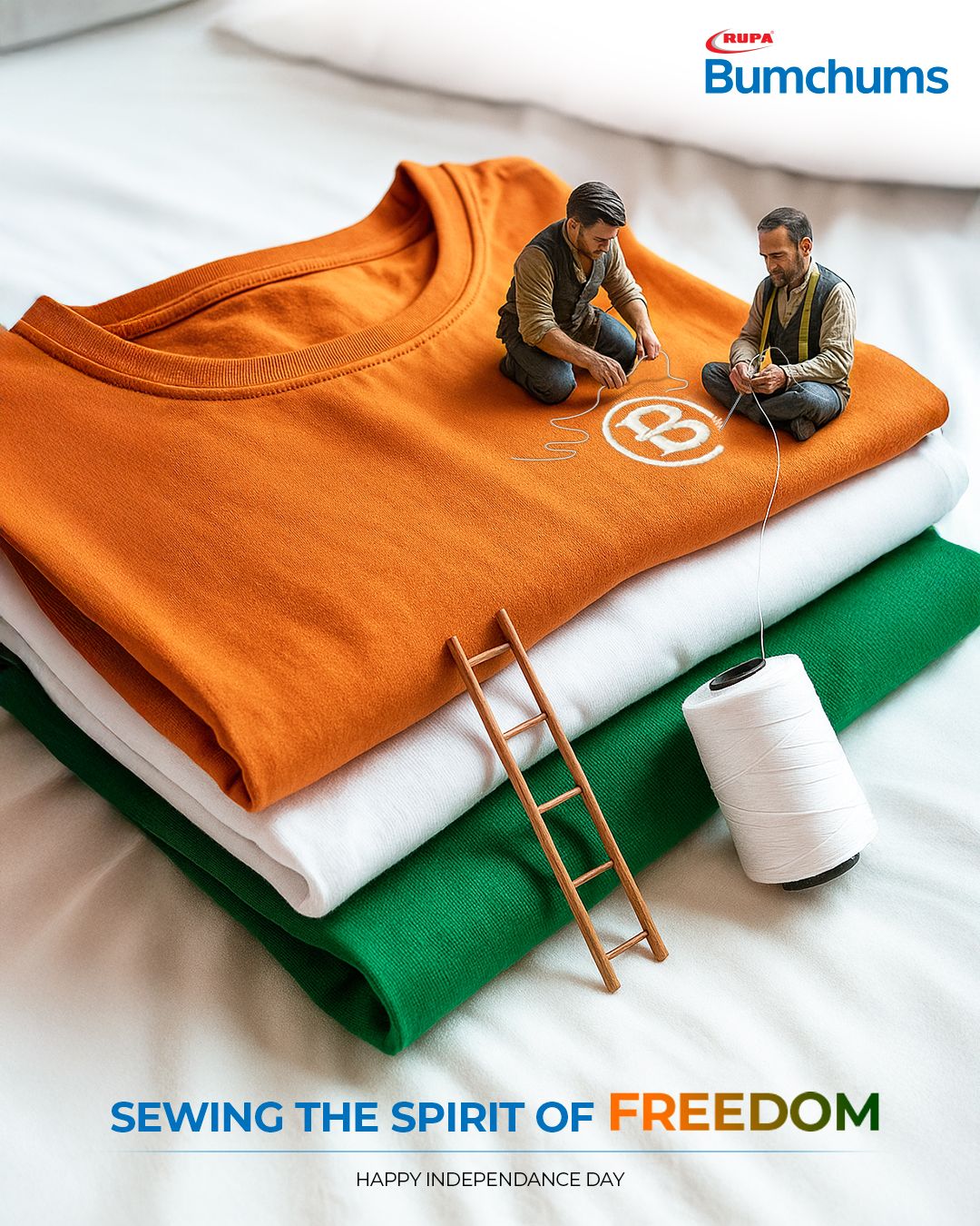 Miniature tailors stitching a logo on stacked saffron, white and green t-shirts