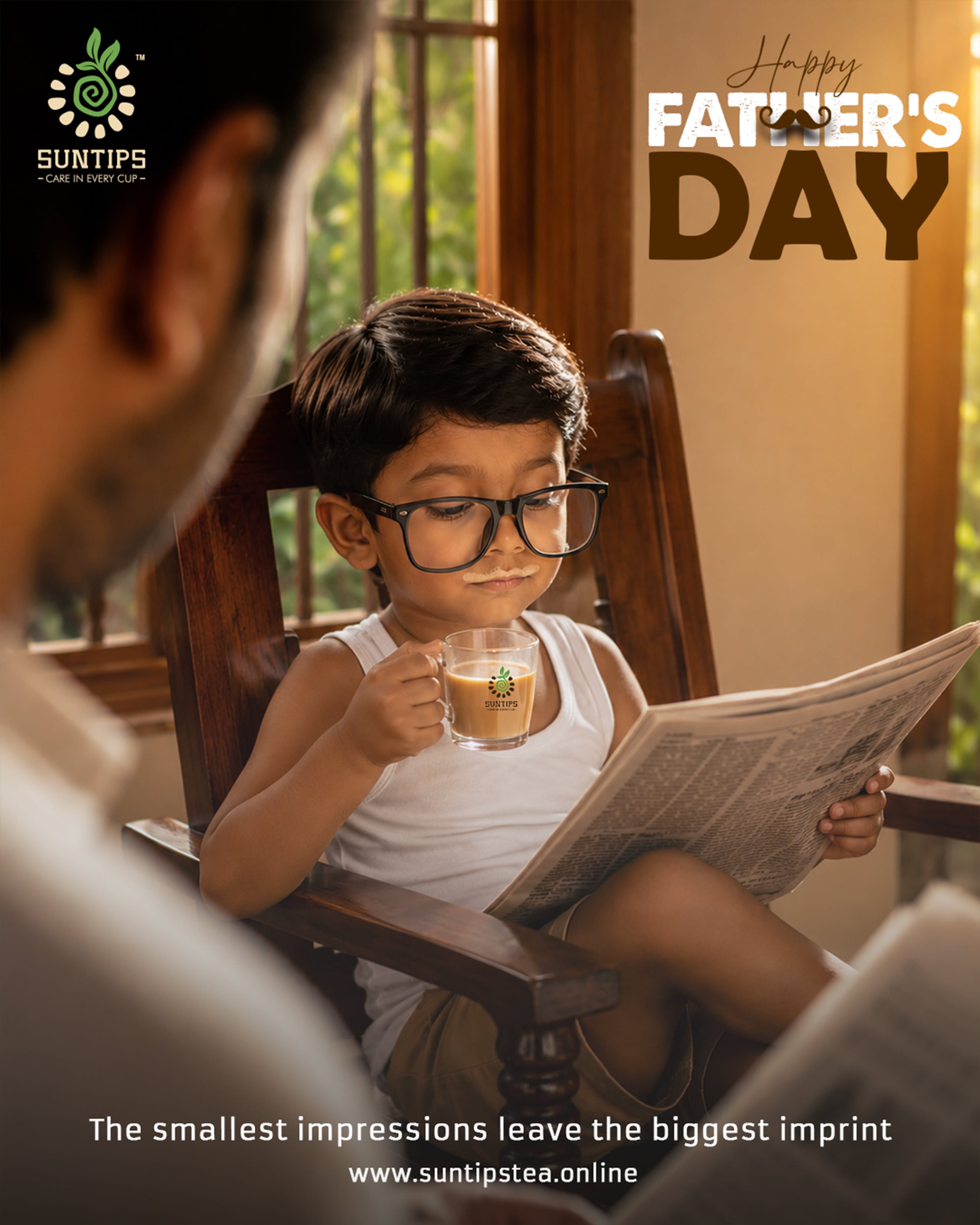 Little boy in big glasses sipping tea and reading a newspaper like his dad