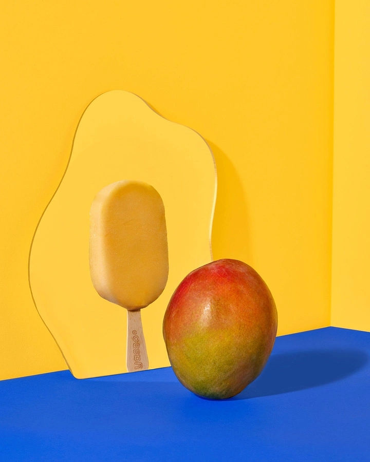 Ice Cream & Gelato creative ad: Mango popsicle reflected in a wavy mirror beside a whole mango