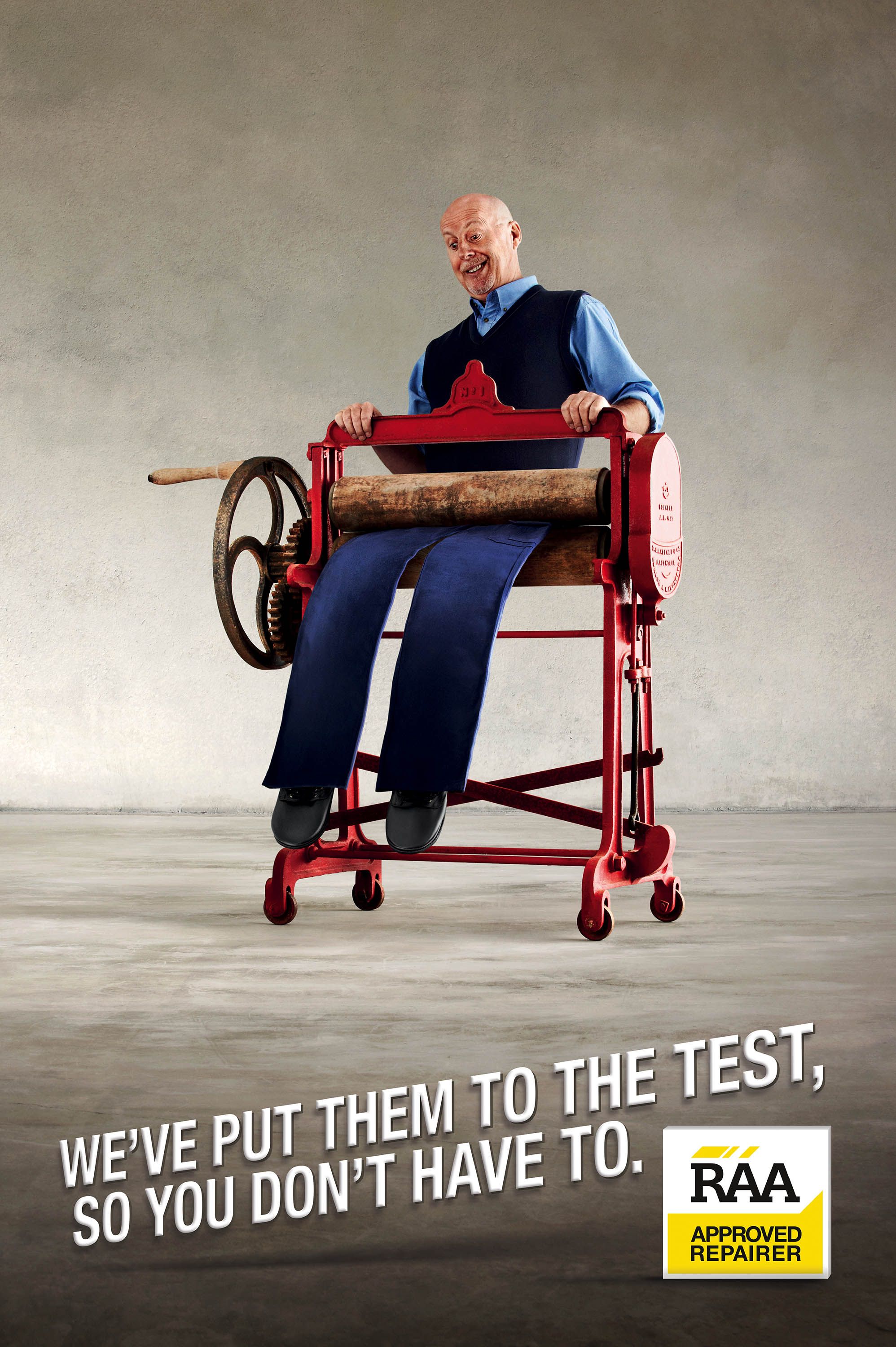 Poster: Bald man grimacing while squeezed through a red antique clothes mangle