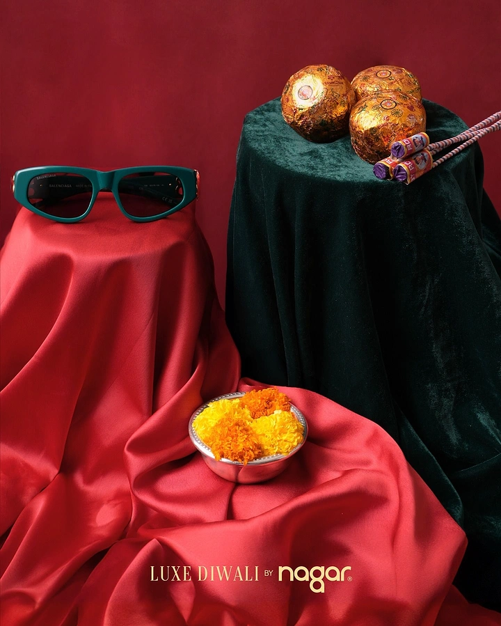 Diwali creative ad: Teal sunglasses on draped red satin with firecrackers and marigold bowl