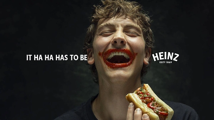Halloween creative ad: Laughing young man with a ketchup-smeared Joker-style grin holding a hot dog