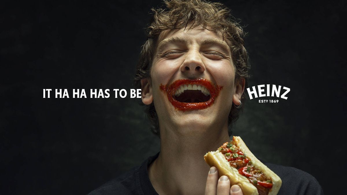 Laughing young man with a ketchup-smeared Joker-style grin holding a hot dog