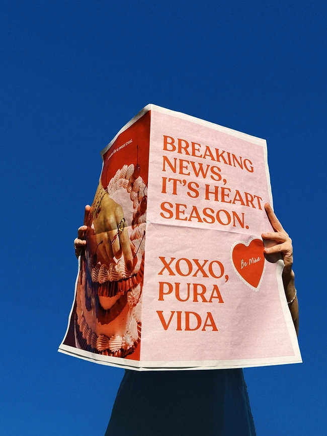 Valentine's Day creative ad: Person holding up a pink newspaper against a blue sky