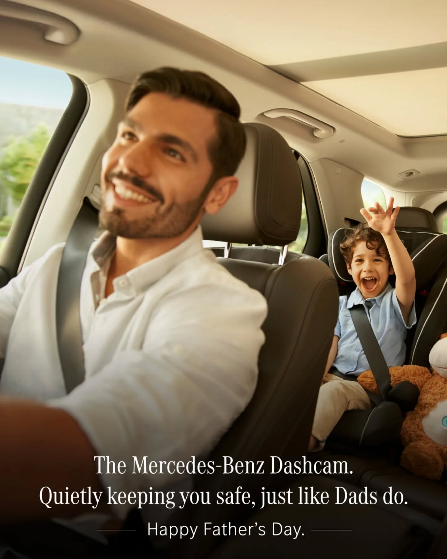 Smiling father driving while an excited son waves from a rear car seat