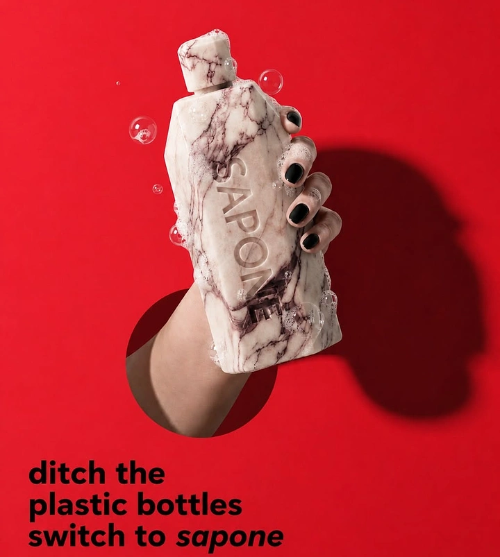 Soap & Bath Products creative ad: Hand bursting through a hole holding a marble-carved soap bottle