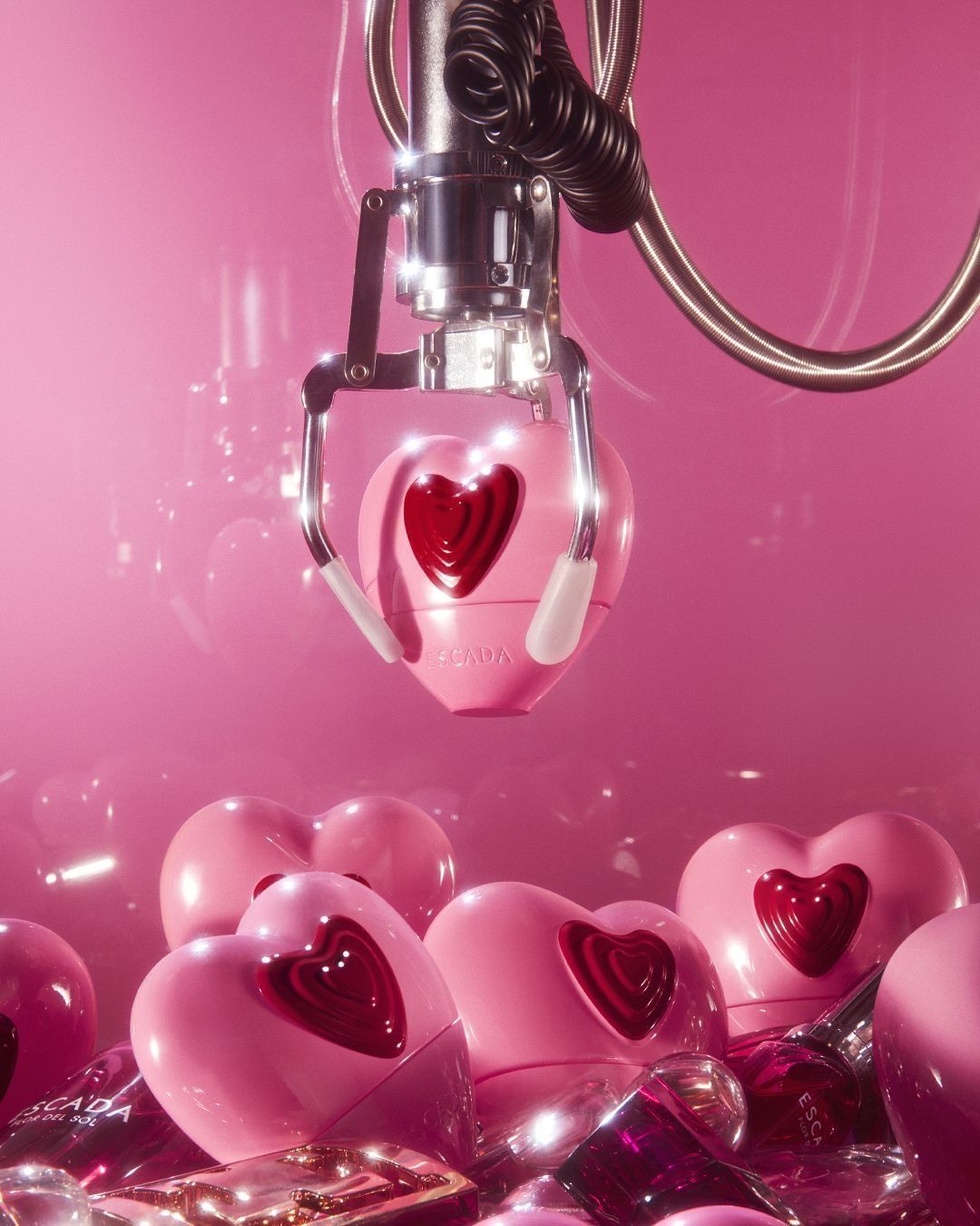 Claw-machine claw lifting a pink heart-shaped perfume bottle