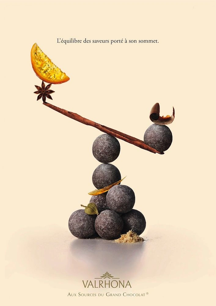 Creative ad: Stacked cocoa truffles balancing a cinnamon-stick seesaw with spices