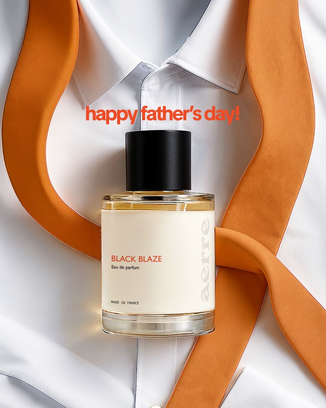Perfume bottle laid on a crisp white shirt with a looping orange tie