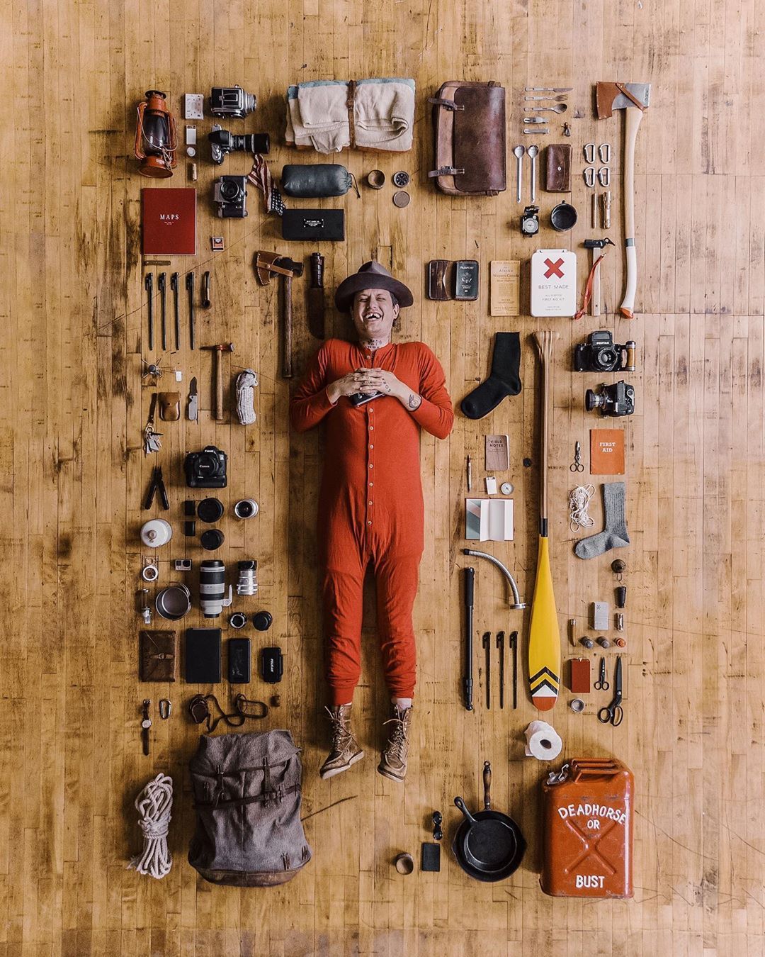 Instagram post: Laughing man in red union suit amid knolled camping gear