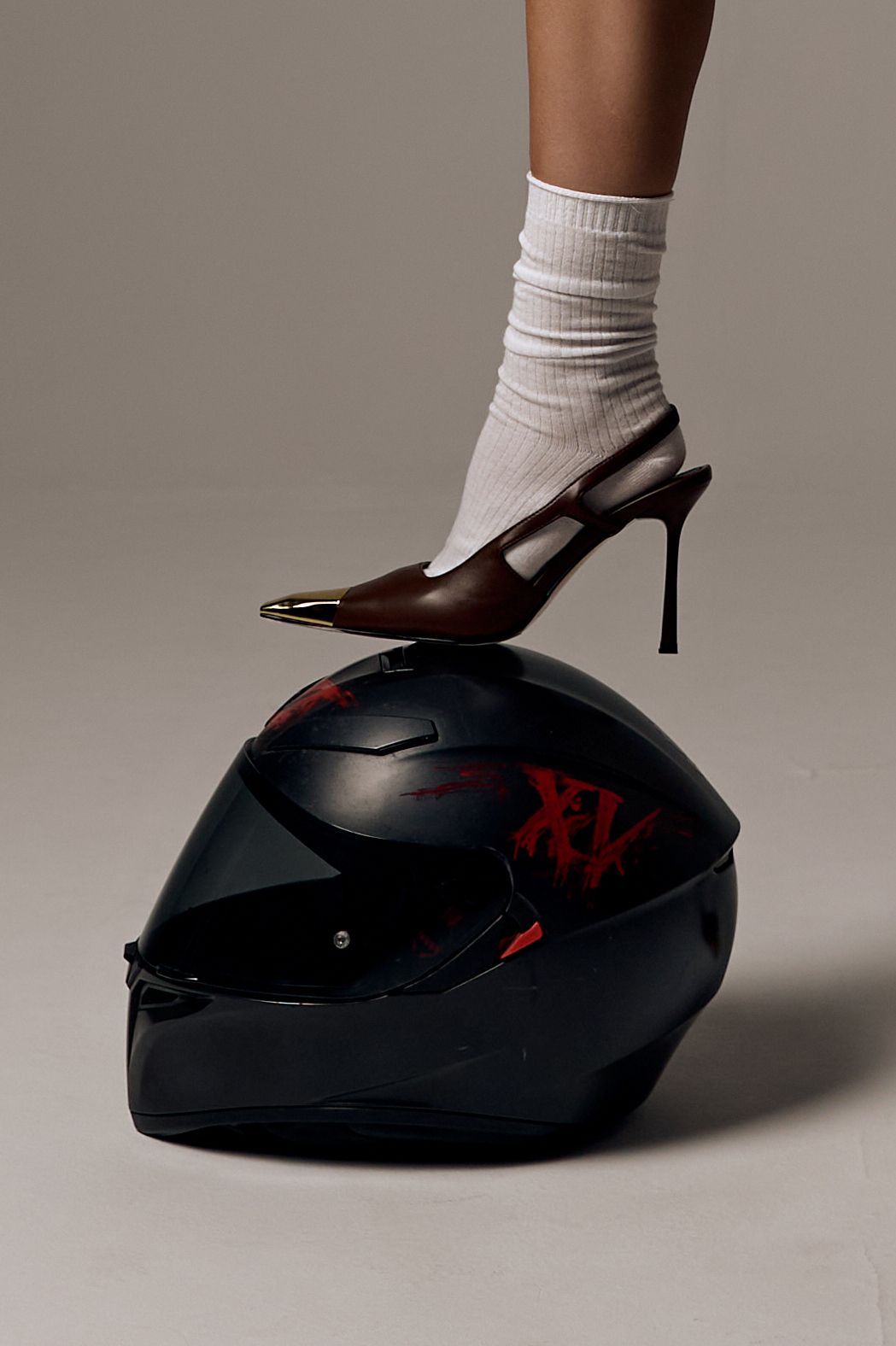 Instagram post: Leg in brown metal-toe slingback heel and white sock resting on a black motorcycle helmet