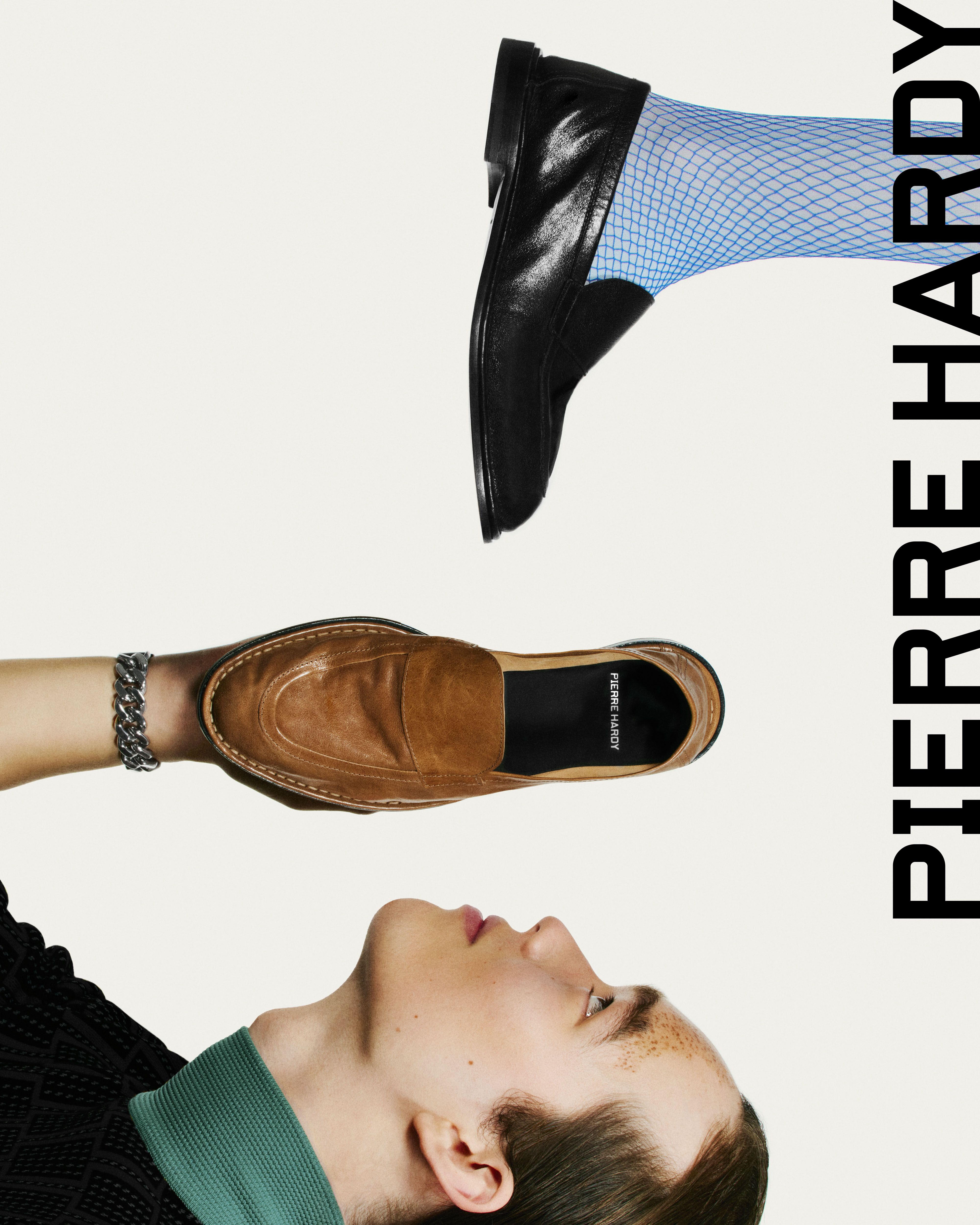 Instagram post: Model balancing a tan loafer on a hand beneath a floating black loafer on a blue fishnet-socked foot