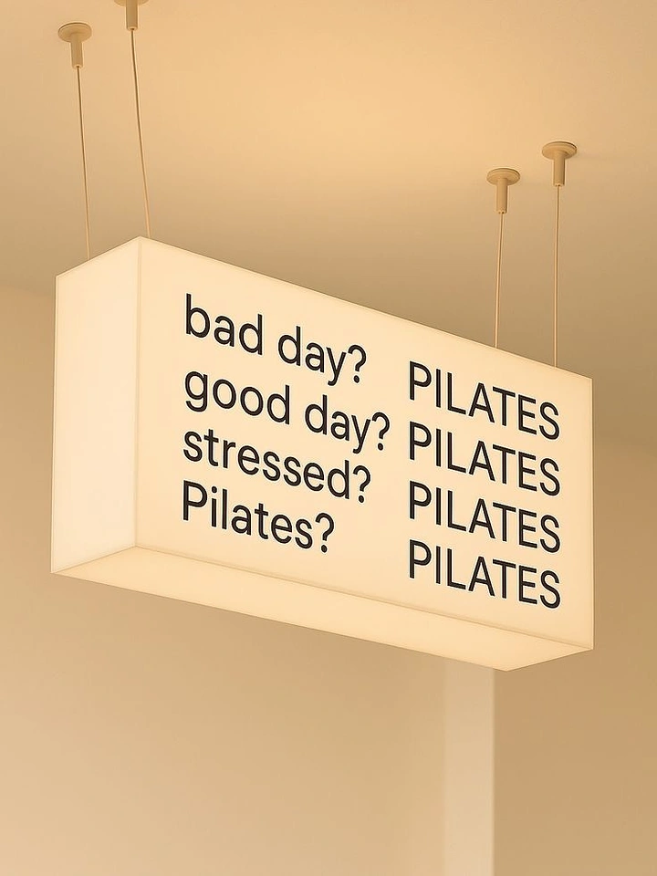 Pilates Studios creative ad: Suspended glowing lightbox sign with a humorous Pilates text list