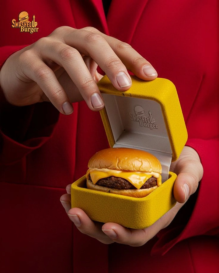 Restaurant & Cafe creative ad: Mini cheeseburger inside an open yellow velvet ring box held in hands