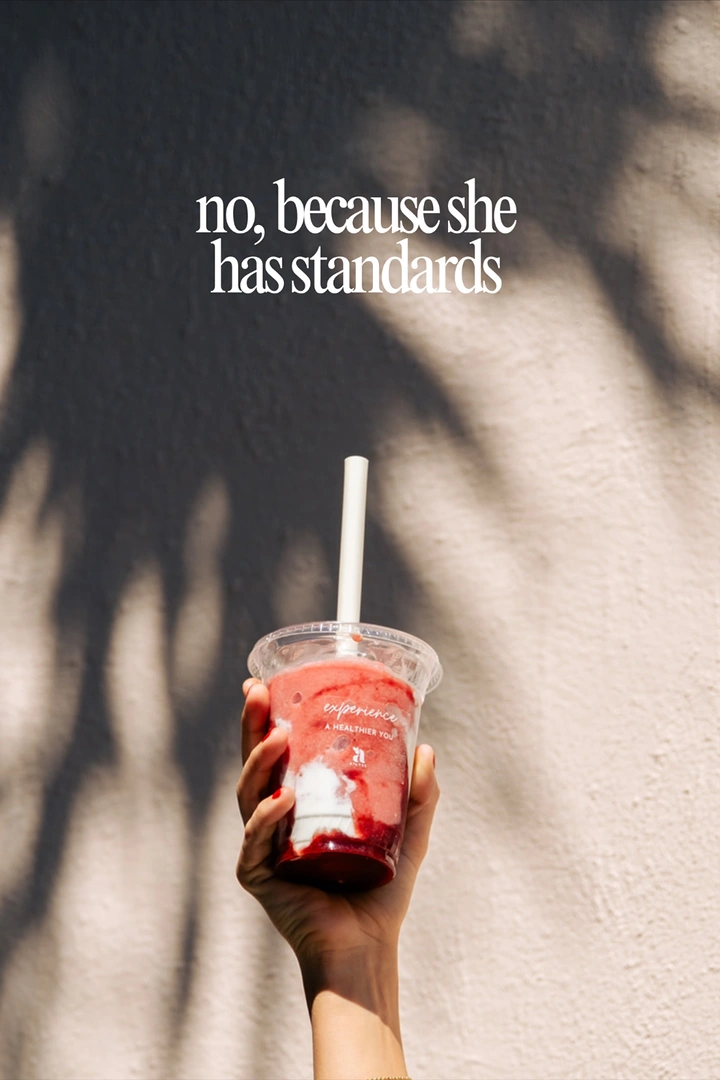 Juice Bars & Smoothies creative ad: Hand raising a branded berry smoothie cup against a sunlit wall with palm shadows