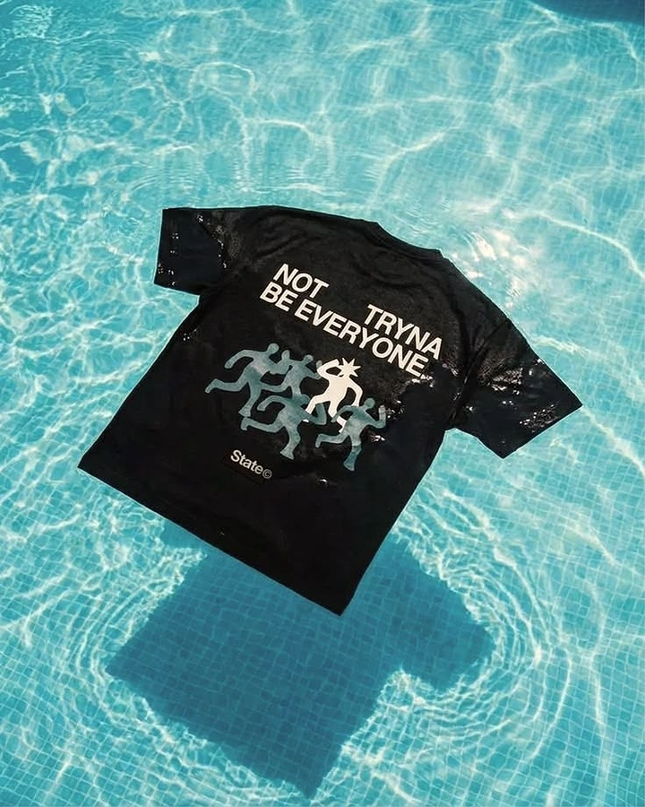Print-on-Demand & Merch creative ad: Black graphic t-shirt floating flat on a pool surface