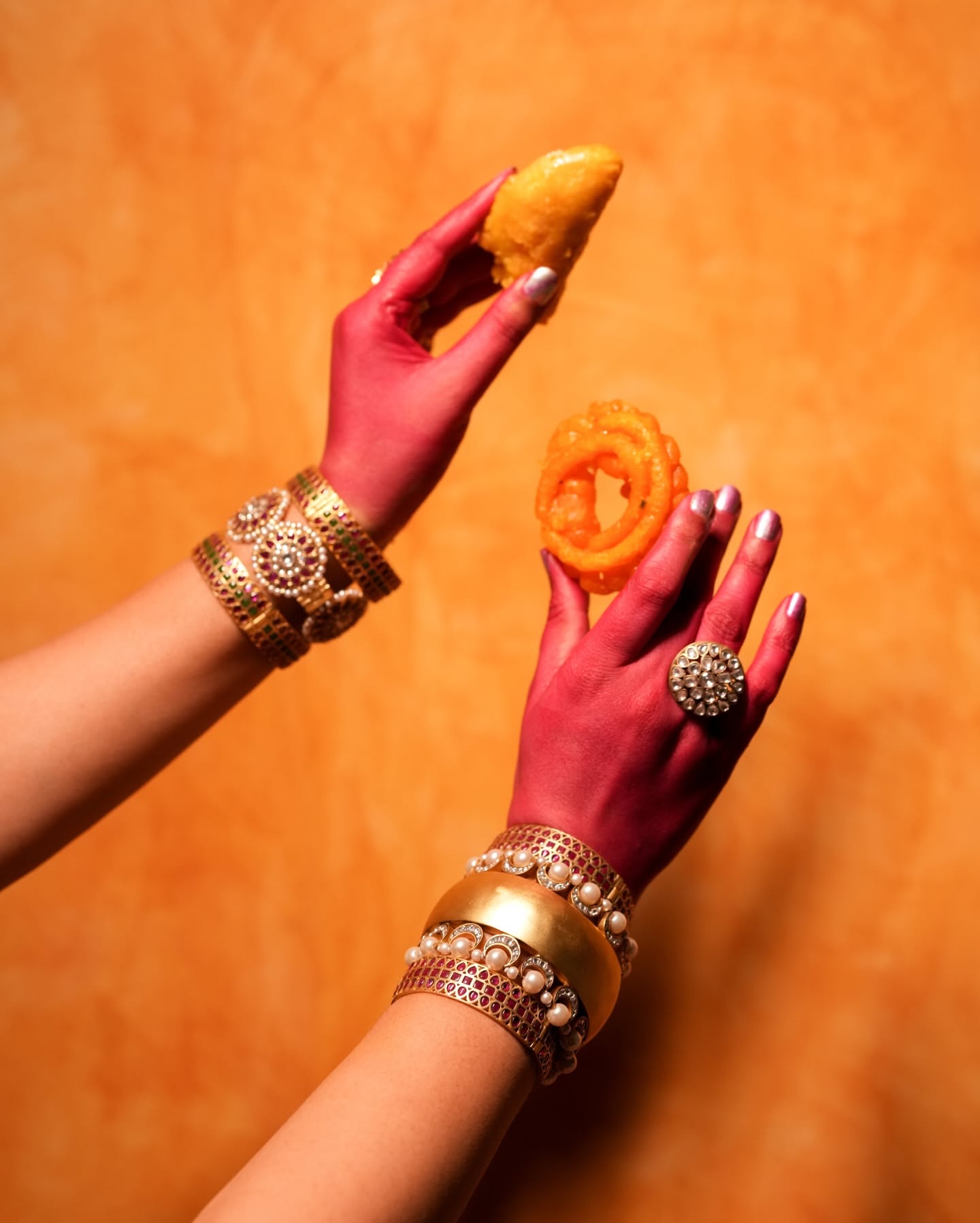 Holi Carousel: Jewelled hands with pink-stained skin holding a jalebi and a sweets platter, slide 2