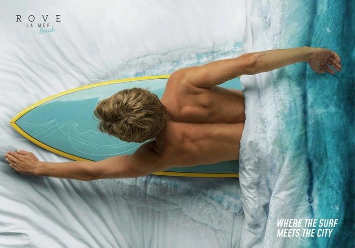 Hotel & Hospitality creative ad: Man lying on a surfboard in bed, with the sheets turning into an ocean wave