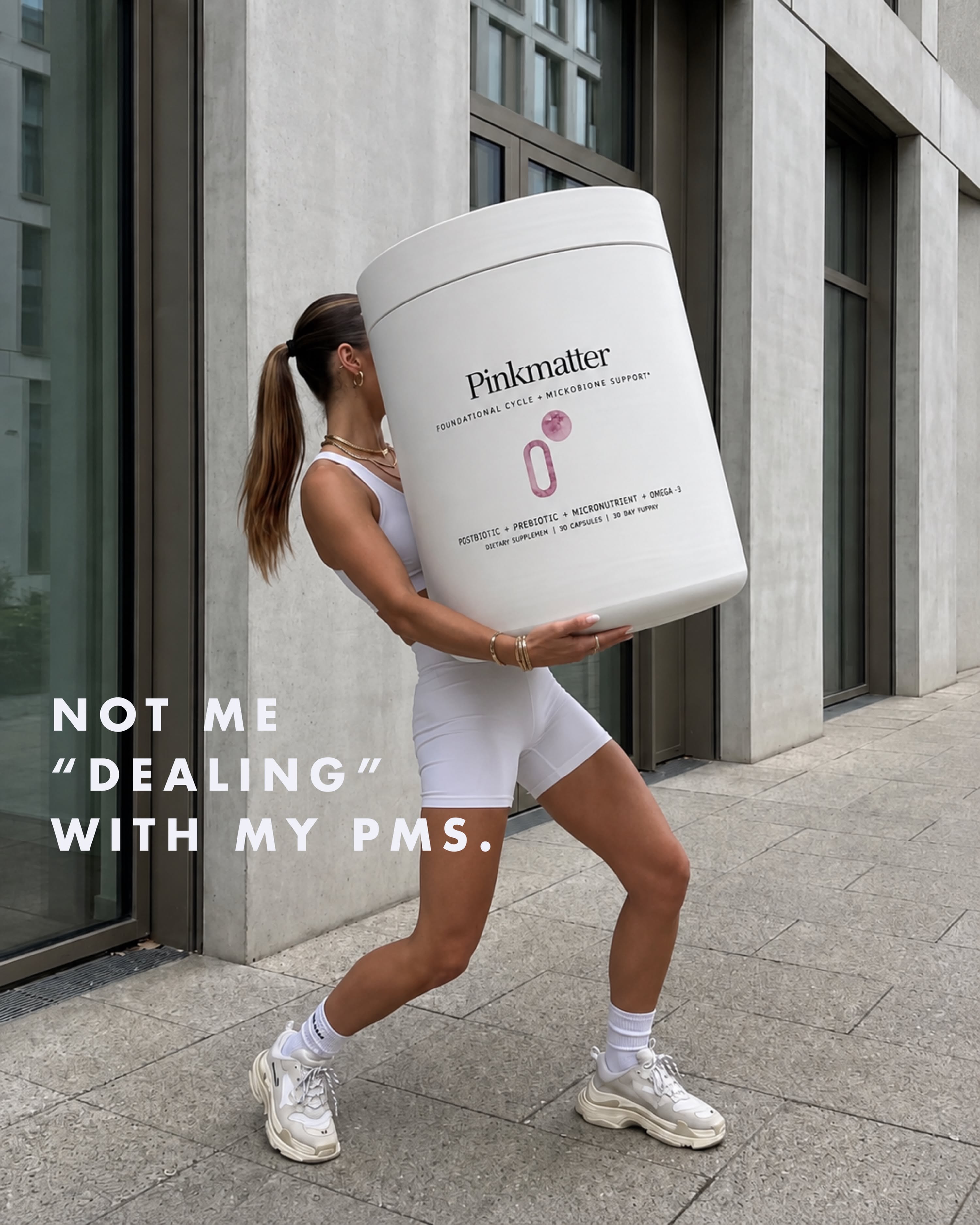 Instagram post: Woman in white activewear straining to carry a giant supplement tub