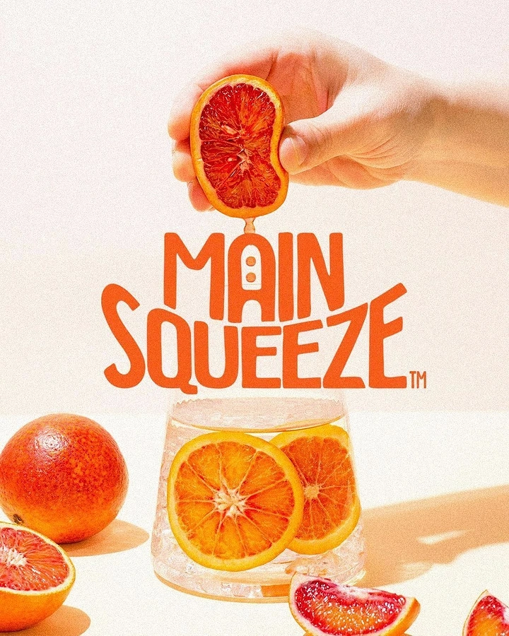 Soft Drinks & Beverages creative ad: Hand squeezing a blood orange half over a glass of iced citrus slices